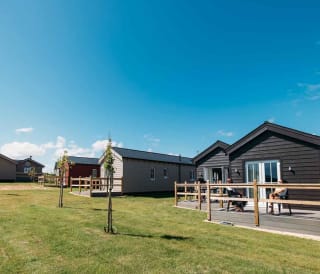 A bright sunny day at our static caravan holiday park in Bay Filey, Yorkshire. In the photo is a row of wooden static caravans next to a grass communal lawn.