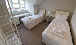 A twin room in one of our cottages. Within the room are two single beds, clothes hanging area, a bedside table with a lamp and a vanity unit below the window. image