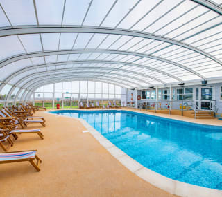A view of the indoor swimming pool at our Essex holiday park, Mersea Island. Multicoloured deck chairs can be seen around the pool. image