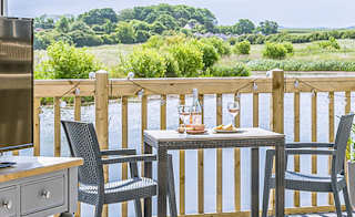 The lounge area of The Meadow Lakeside Lodge at The Bay Filey, which leads out to the decking area overlooking the lake on a sunny day. image