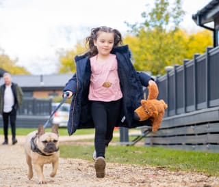 A young girl running towards the camera with a dog on the lead at one of our UK holiday parks.