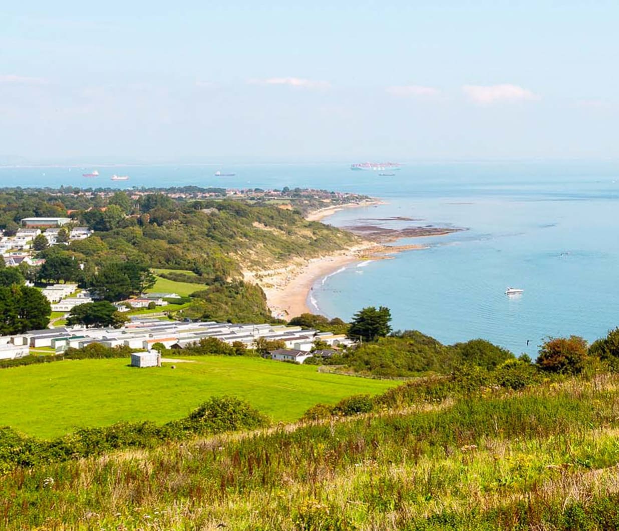 A view of our Whitecliff Bay holiday park. The cliffs are overlooking the sea, with plenty of boats cruising around. The coastline stretches far into the distance.