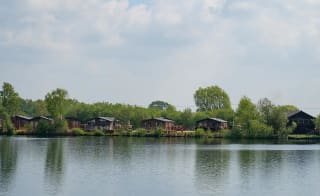 A panoramic view of a river with wooden lodges and trees at one of our holiday parks in Lincolnshire. image
