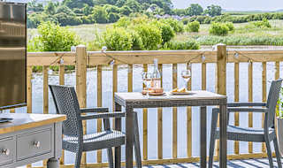 The lounge area of The Meadow Lakeside Lodge at The Bay Filey, which leads out to the decking area overlooking the lake on a sunny day. image