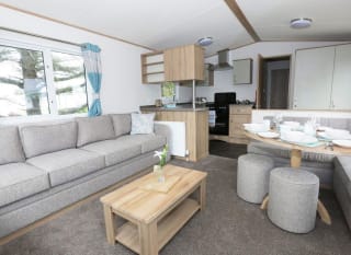 Suggested: The interior of one of our luxury caravans. There's a large, grey sofa, a seating area with a table, and a kitchen space with several appliances. image