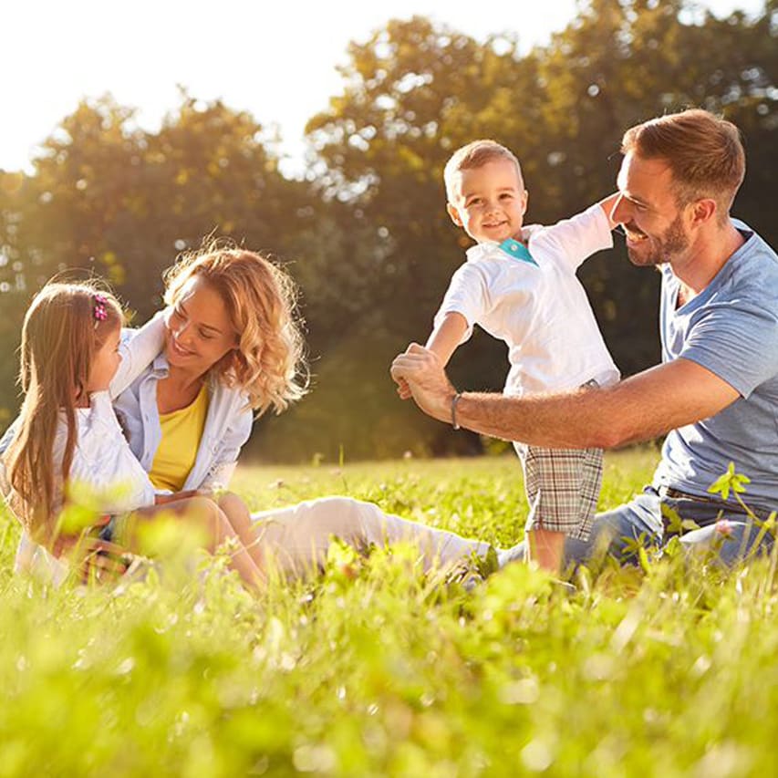 A young family playing in the grass outside on a sunny day.