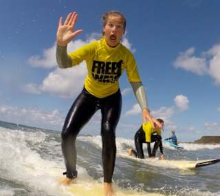 A girl surfing in the sea whilst waving at the camera. image