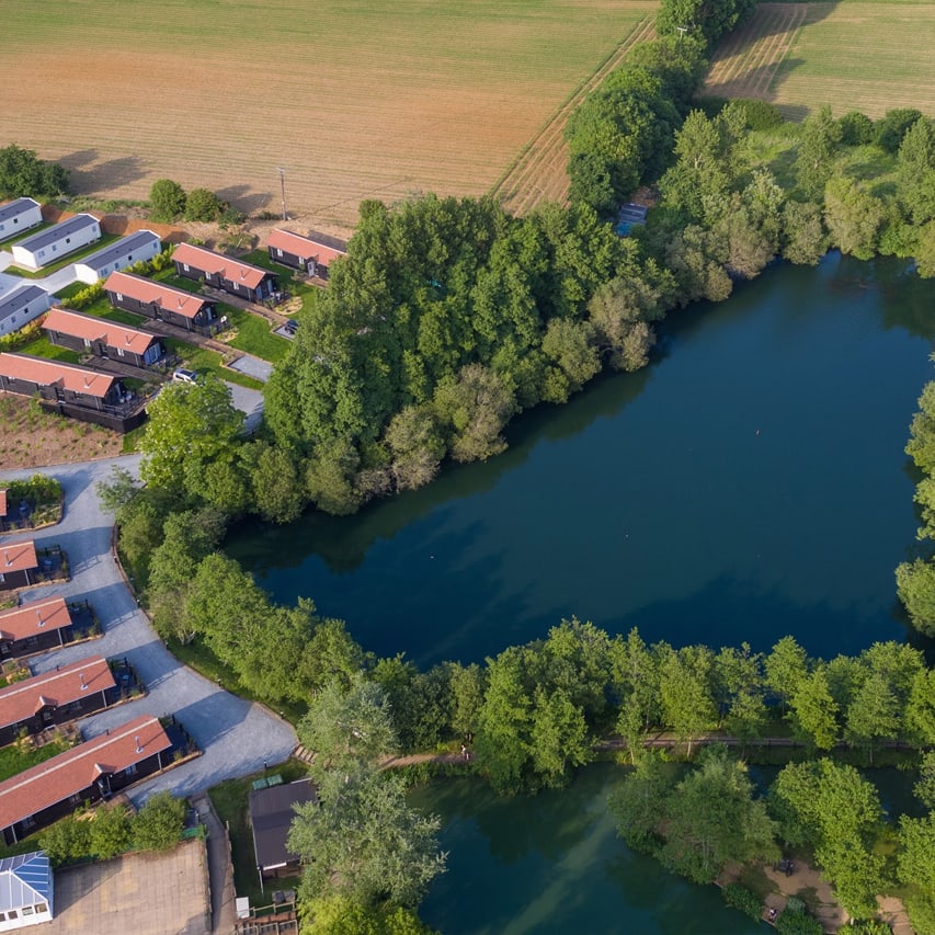 An aerial view of a lake with holiday homes surrounding the lake, with caravans in the distance.