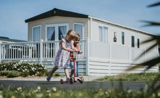 A child riding on their scooter outside one of our stunning holiday homes at Newperran Holiday Resort, Cornwall, on a summers day. image