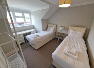 A twin room in one of our cottages. Within the room are two single beds, clothes hanging area, a bedside table with a lamp and a vanity unit below the window. image