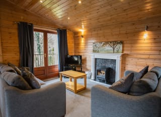 The interior of one of our woodland style holiday lodges. There's two grey sofas, a TV, and wooden double-doors. image