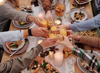 A group of people cheersing over a table of food. image
