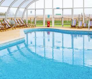 The awesome indoor swimming pool at our holiday park in Essex, Mersea Island. There are multicoloured deck chairs all around the pool.