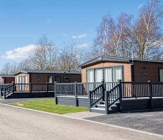A photo of a row of wooden holiday lodges at our holiday park Appletree, Lincolnshire on a cloudy sunny day.