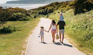 A young family are walking along a dry dirt path which is situated between rolling green hills on a hot summer's day. image