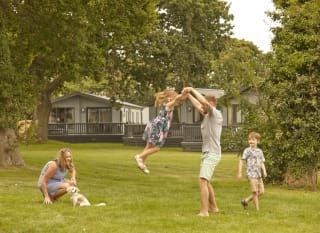 A young family playing outside on a sunny day. There is a row of caravans in the background. image