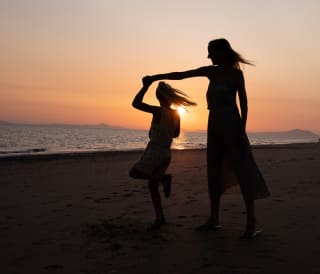 A mother and daughter dancing on the beach at sunset.
