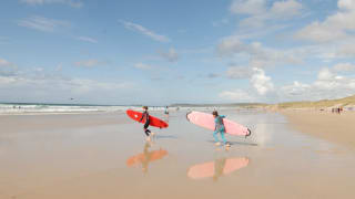 Two children running on the beach with surf boards towards the sea.