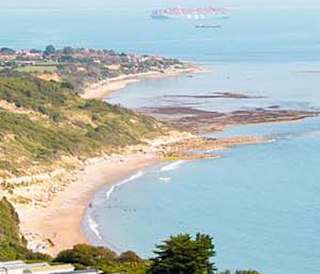 A view of our Whitecliff Bay holiday park. The cliffs are overlooking the sea, with plenty of boats cruising around. The coastline stretches far into the distance.