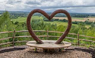 A panoramic view of the countryside, with a viewing area in the foreground. The bench features a wooden heart arch. image