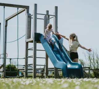 A child going down the slide at our adventure playground at Newperran Holiday Park. There is a woman standing next to the slide. image