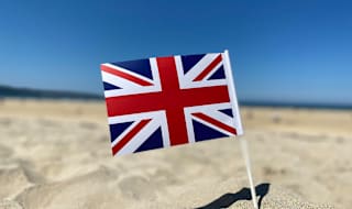 A union jack flag in the sand on a sunny day.