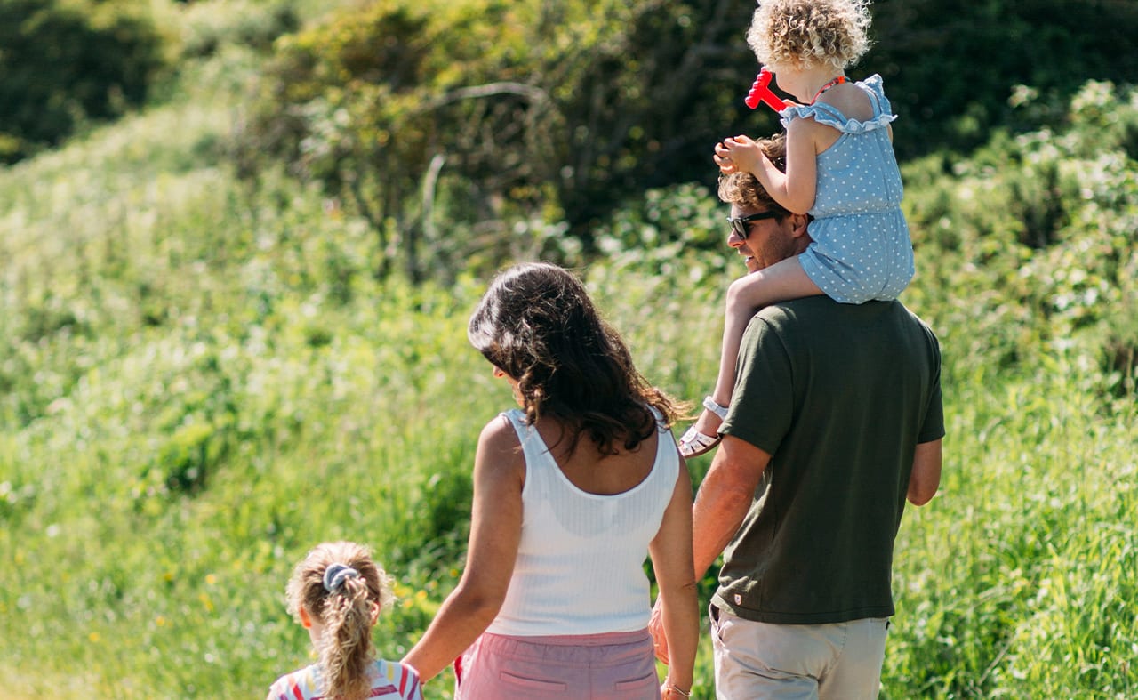 Back shot of family of four walking together, young girl on dad's shoulders and other young girl holding mother's hands. image