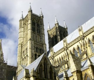 A photo of the Lincoln cathedral taken from below looking up at one of the spires on a cloudy day.
