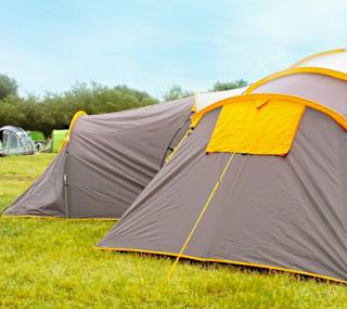 A shot of the back of two grey and yellow pitched up tent on some grass. image