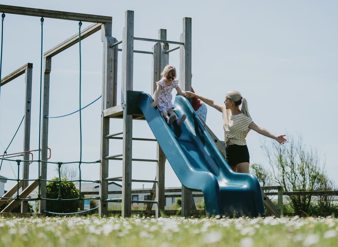 A child going down the slide at our adventure playground at Newperran Holiday Park. There is a woman standing next to the slide. image