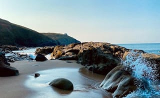 An image of a wave crashing into rocks on the beach. image