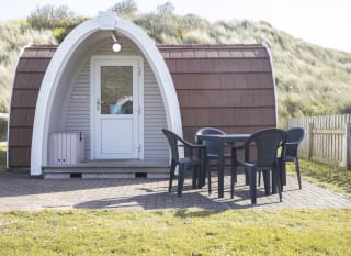 Exterior of our camping pod at St Ives Bay, Cornwall. A table and chair is located on the right, the perfect spot for brunch in the sunshine. image