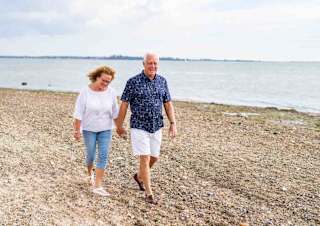 A mature hetero white couple are walking along the sands of Mersea Island beach, Essex.