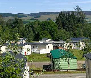 Our Moffat Manor holiday park. There are several luxurious holiday homes onsite, with tall trees and hills in the background.