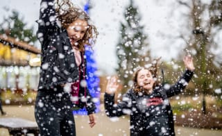 Two girls with long brown hair wearing navy blue coatsare jumping in the air excitedly and laughing as the heavy snowfall lands around them. image