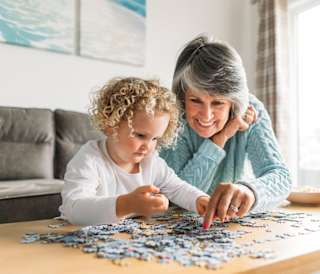 A grandma and granddaughter completing a puzzle together.
