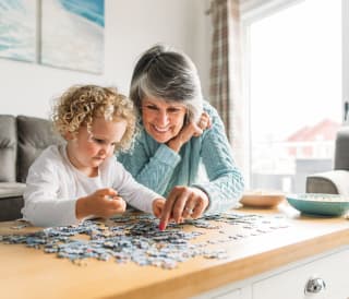 A grandma and granddaughter completing a puzzle together.