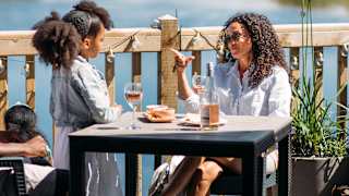 Mother and young daughter sitting lakeside enjoying lunch and drinks together in the sunshine.
