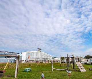 The outdoor adventure playground at our Essex holiday park, Mersea Island. There is views of the indoor swimming pool conservatory and some caravans in the background.