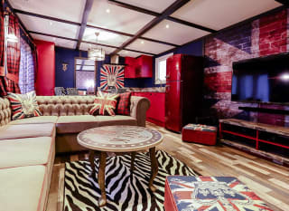 The interior of The Rockstar holiday home. There's a variety of luxurious furniture, each with a British rockstar theme and colour. There's a long, cream sofa, a TV, and a red fridge in the spacious kitchen. image