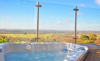 A closeup photo of an outdoor hot tub next to glass fencing on a bright sunny day at out holiday park in Sandy Balls, Hampshire. image