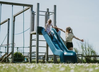 A child going down the slide at our adventure playground at Newperran Holiday Park. There is a woman standing next to the slide. image
