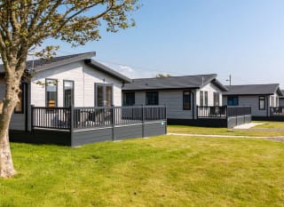 Our amazing lodges at one of our holiday parks. There are three luxury lodges surrounded by green grass, and the sun is shining down. image