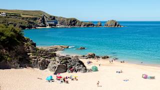 An aerial view of Padstow beach. Holiday goers are on the beach and in the sea. A bright blue sky is above the sea.