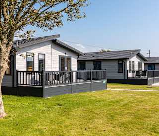 Our amazing lodges at one of our holiday parks. There are three luxury lodges surrounded by green grass, and the sun is shining down.