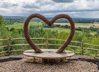 A panoramic view of the countryside, with a viewing area in the foreground. The bench features a wooden heart arch. image