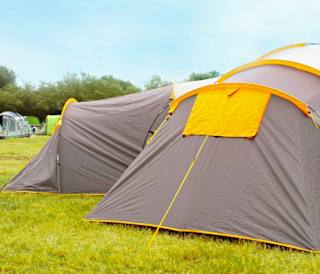 A shot of the back of two grey and yellow pitched up tent on some grass.