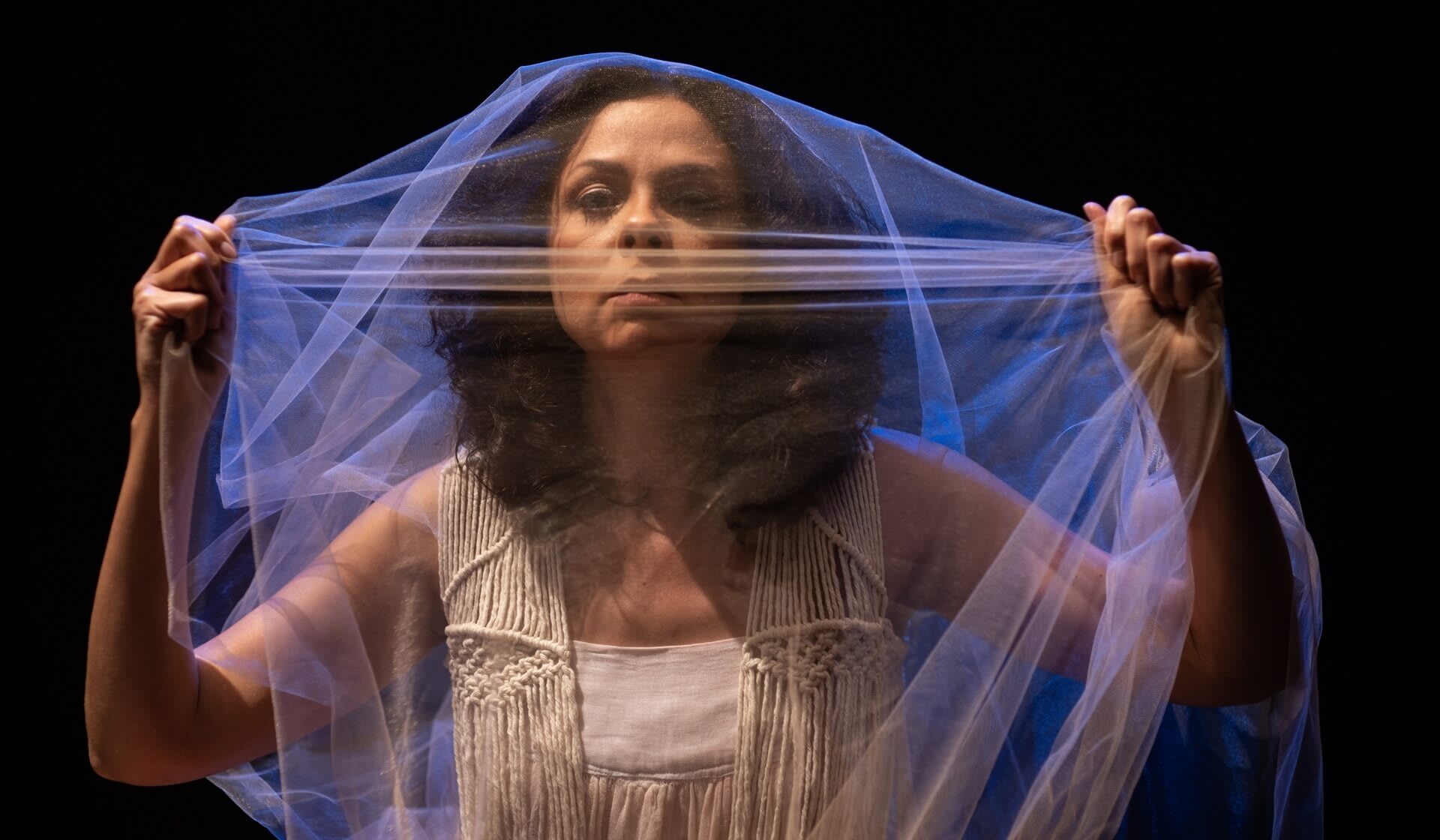 Suzana Nascimento com um véu transparente sob o rosto com fundo preto