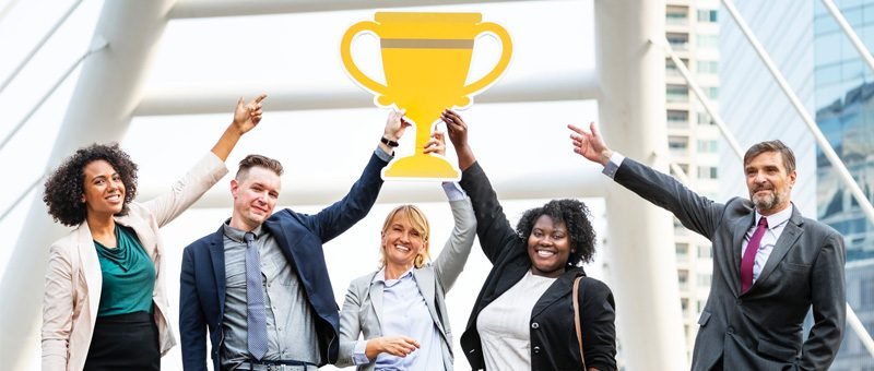 pessoas com terno, funcionaŕios, segurando um trofeú de ouro feito de papelão