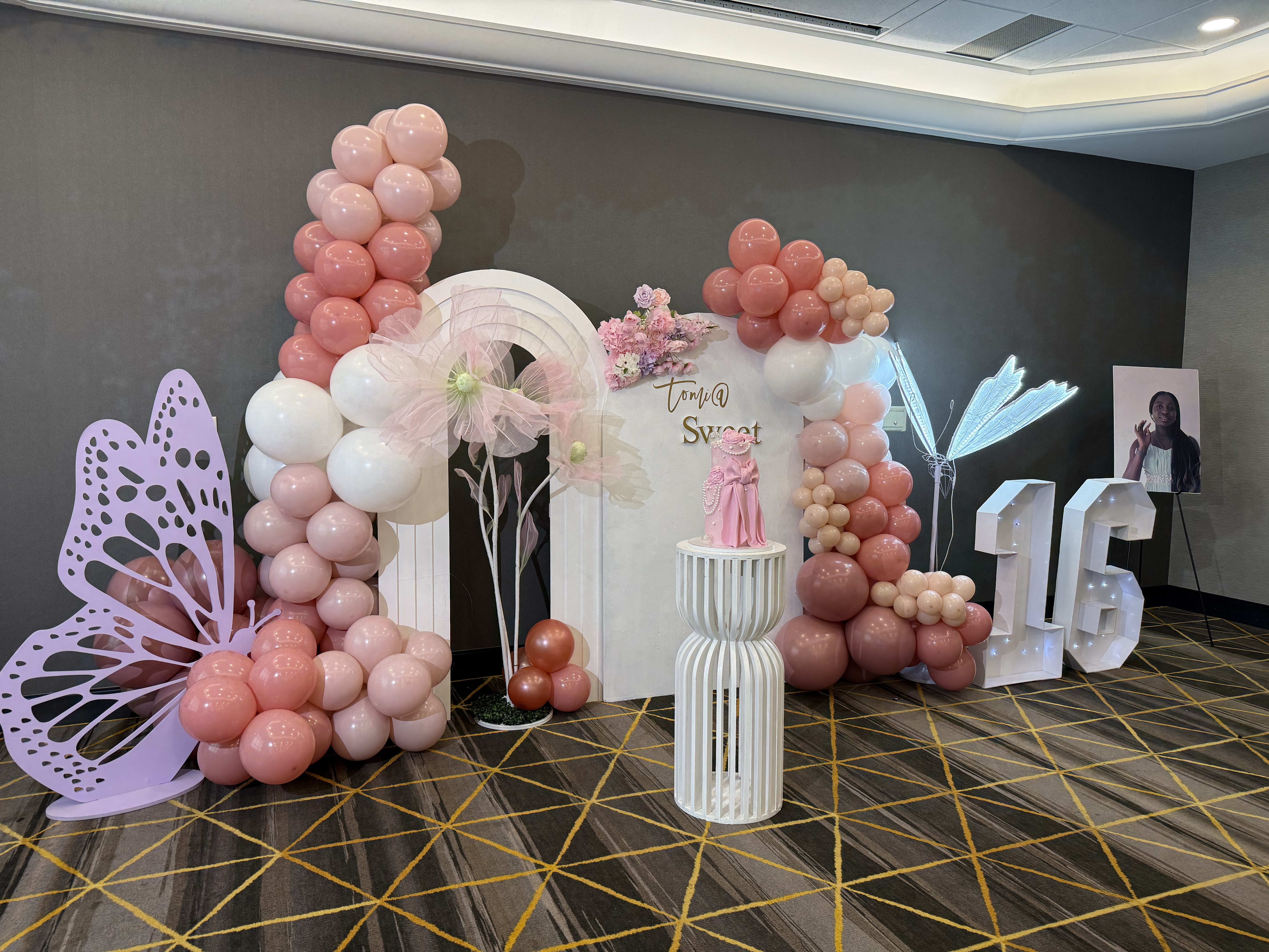 Custom balloon and floral backdrop with pedestal and styled venue lighting
